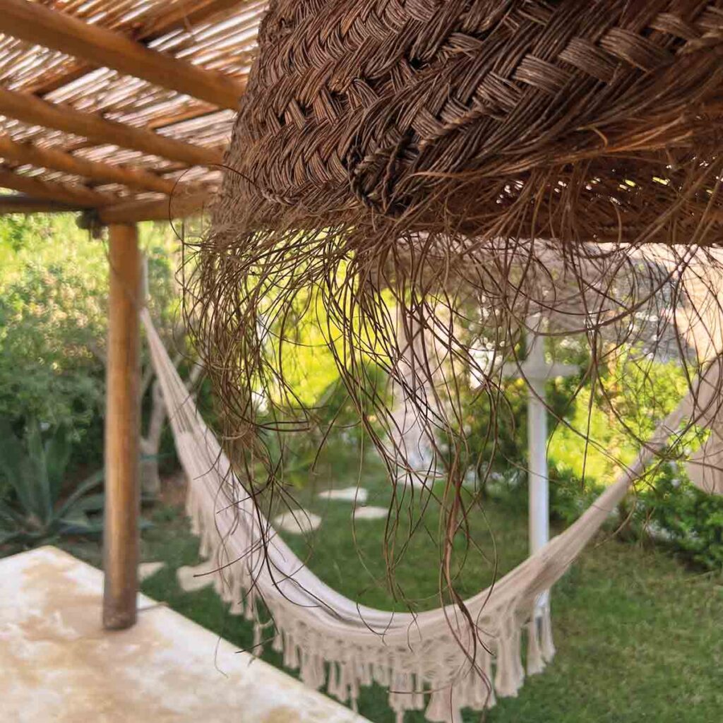 Bastlampe mit ausgefransten Naturfasern unter einer Holzpergola in einem mediterranen Garten in Portugal.