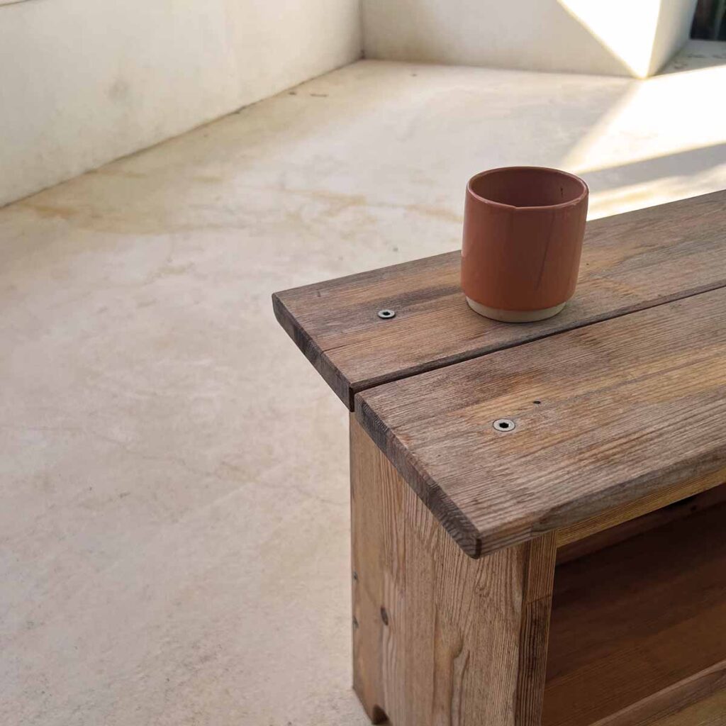 Handgefertigte Keramiktasse auf einer Holzbank vor einer mineralischen Sitzfläche in einem mediterranen Ferienhaus in Portugal.