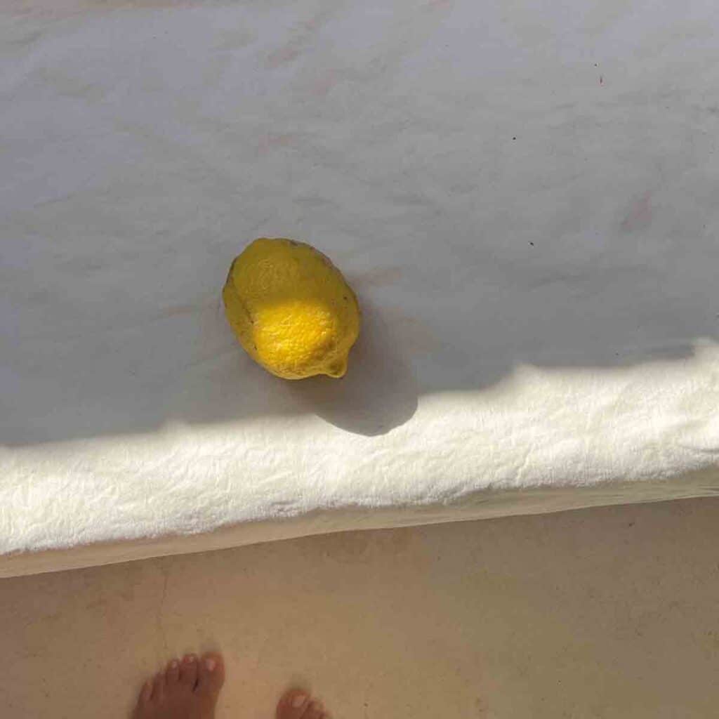 Mediterrane Sitzecke mit mineralischer Sitzbank, Leinenkissen und Zitrone in einem Ferienhaus in Portugal. Naturmaterialien sorgen für echtes Urlaubsgefühl.
